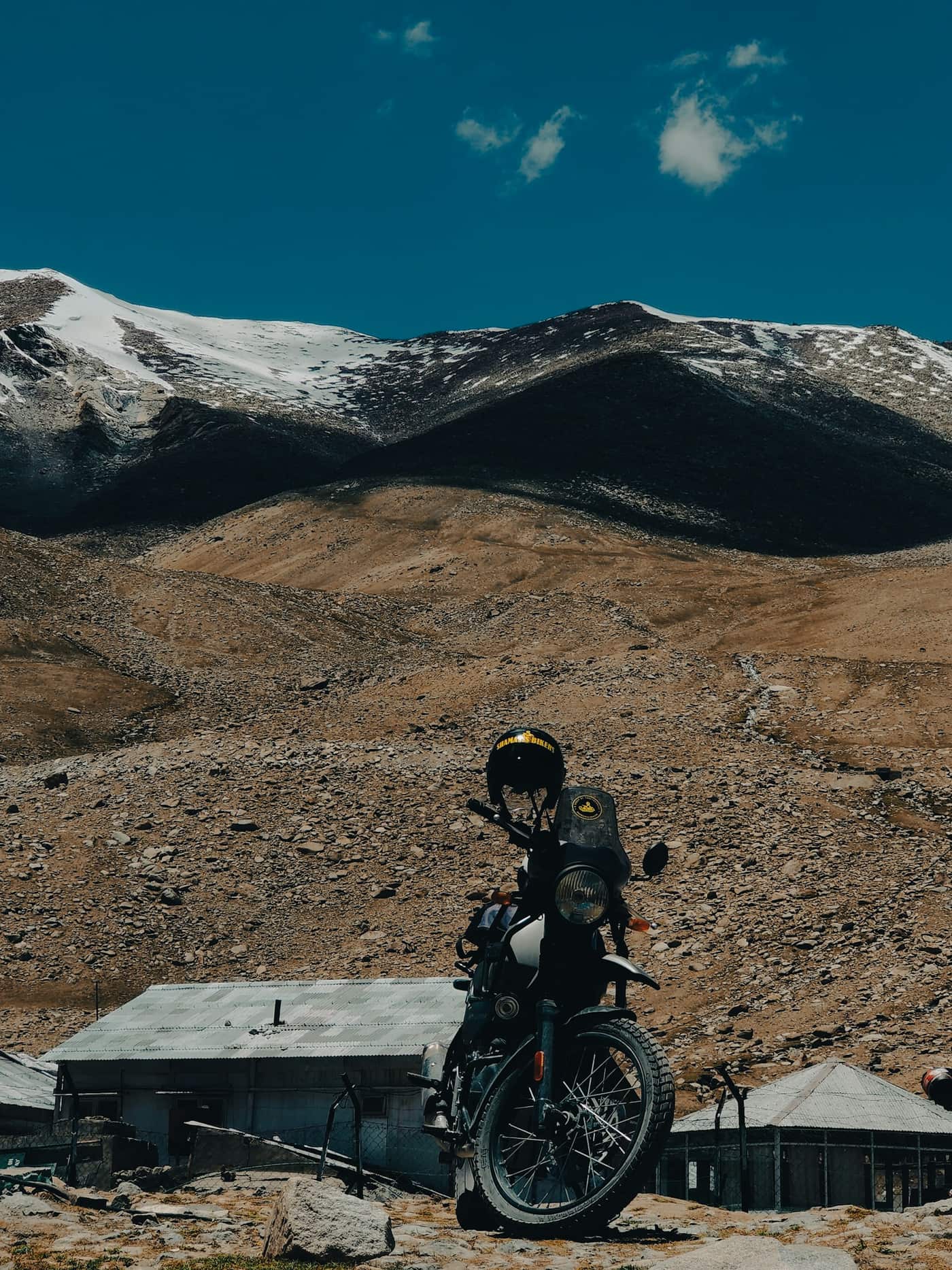 An adventure motorcycle parked on rocky ground with snow-capped mountains behind it.